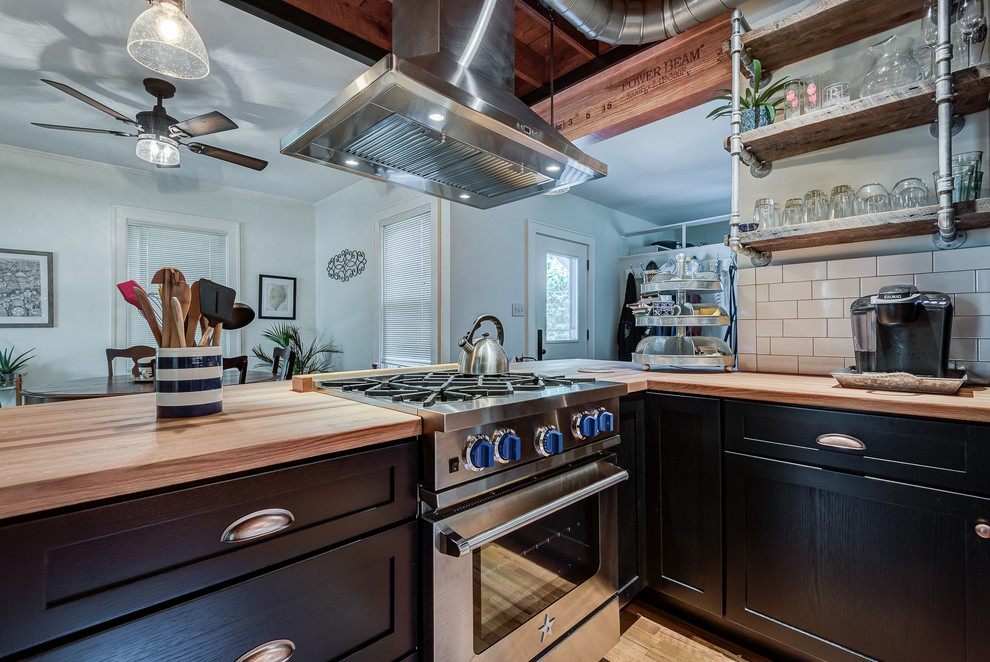 Small urban u-shaped light wood floor eat-in kitchen photo in Chicago with a farmhouse sink, shaker cabinets, black cabinets, wood countertops, white backsplash, stainless steel appliances, a peninsula and subway tile backsplash
