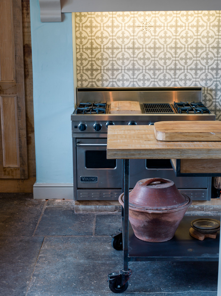 Photo of a large rustic u-shaped kitchen/diner in Wiltshire with a belfast sink, shaker cabinets, distressed cabinets, wood worktops, stainless steel appliances, slate flooring and an island.