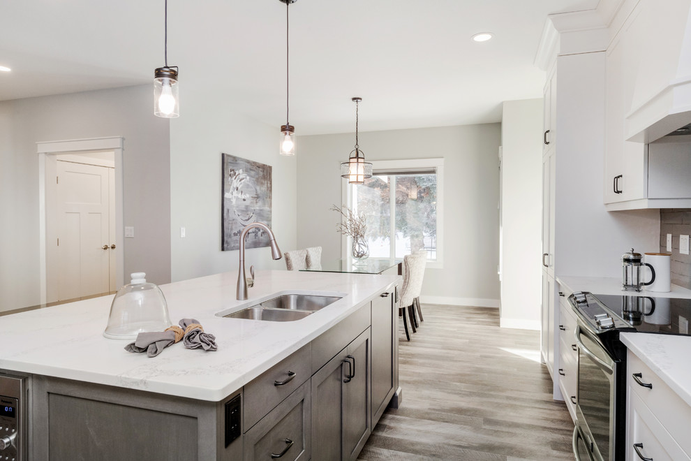 Small transitional single-wall vinyl floor and brown floor open concept kitchen photo in Other with an undermount sink, shaker cabinets, white cabinets, quartzite countertops, gray backsplash, subway tile backsplash, stainless steel appliances and an island