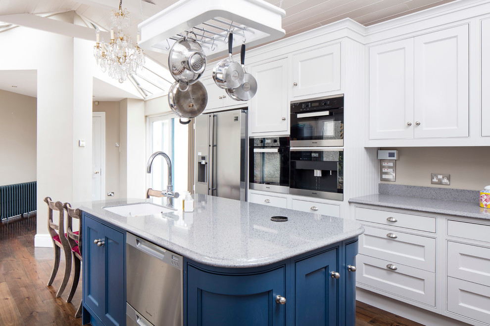 Photo of a large contemporary u-shaped open plan kitchen in Dublin with a submerged sink, recessed-panel cabinets, blue cabinets, composite countertops, stainless steel appliances, medium hardwood flooring and an island.