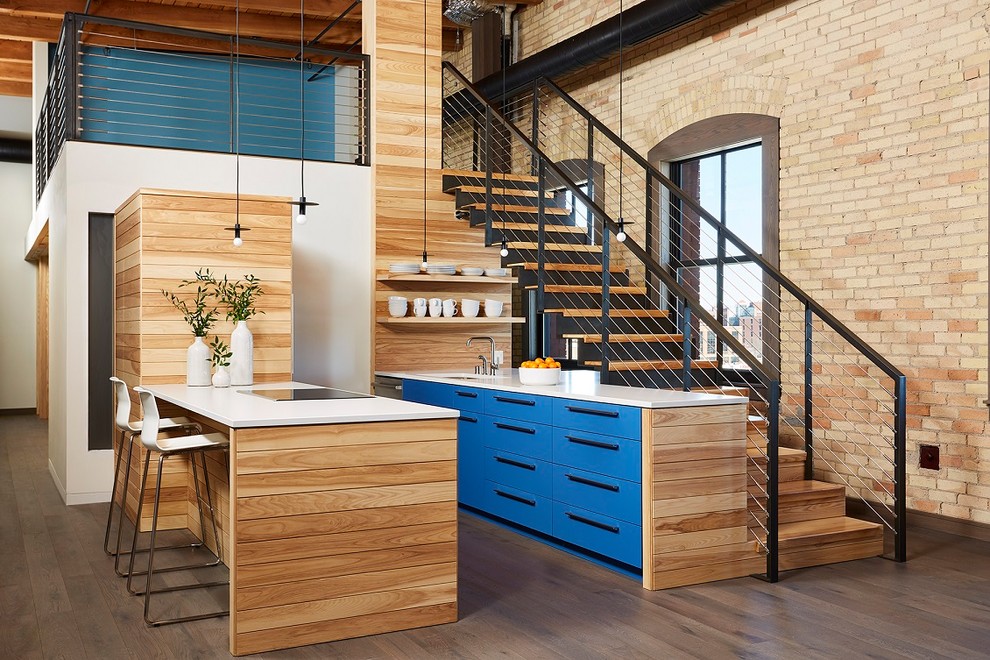 Foto di una cucina parallela minimal con ante blu, lavello sottopiano, ante lisce, paraspruzzi marrone, paraspruzzi in legno, elettrodomestici in acciaio inossidabile, parquet scuro, pavimento marrone e top bianco
