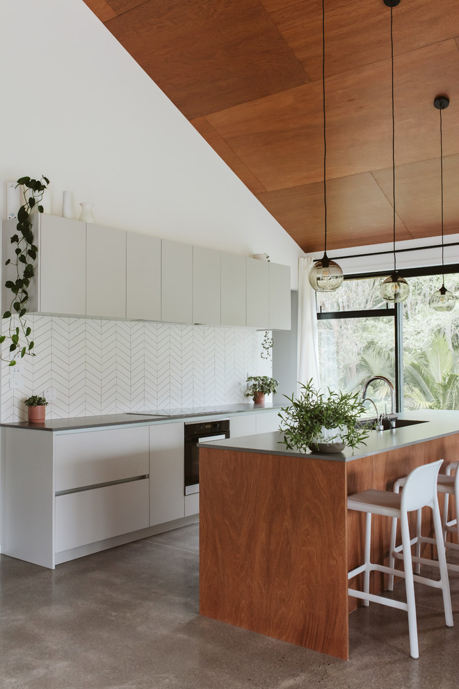 Свежая идея для дизайна: параллельная кухня в современном стиле с врезной мойкой, плоскими фасадами, белыми фасадами, белым фартуком, бетонным полом, островом, серым полом и серой столешницей - отличное фото интерьера