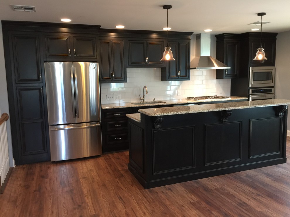 This is an example of a medium sized classic single-wall open plan kitchen in Philadelphia with a submerged sink, beaded cabinets, black cabinets, granite worktops, white splashback, metro tiled splashback, stainless steel appliances, light hardwood flooring and an island.