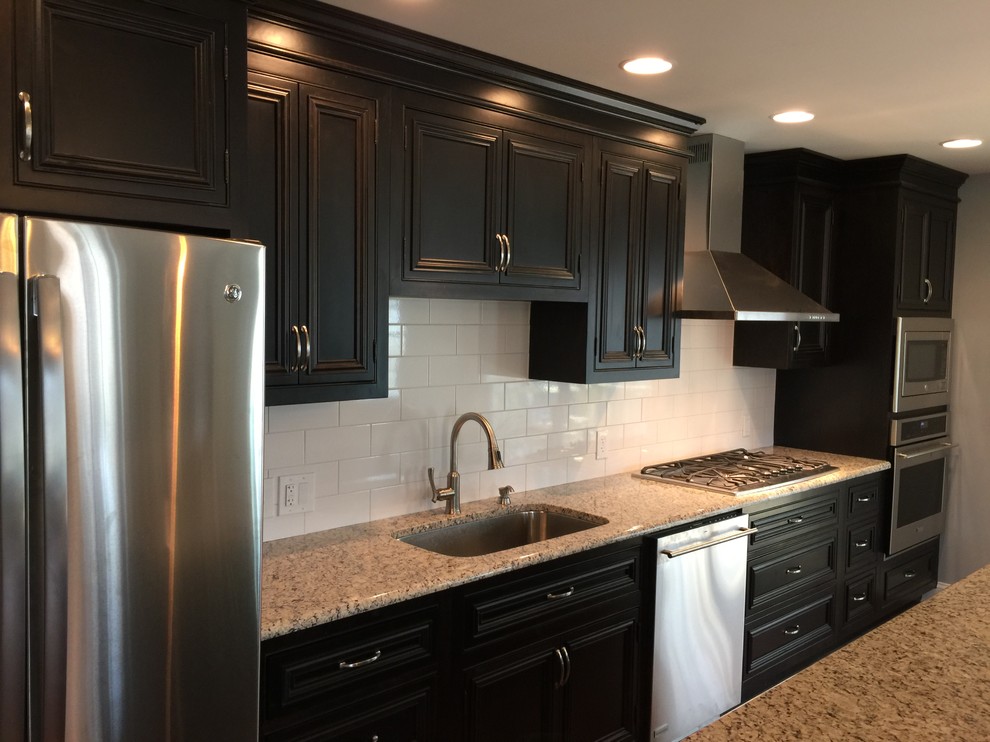 Photo of a medium sized traditional single-wall open plan kitchen in Philadelphia with a submerged sink, beaded cabinets, black cabinets, granite worktops, white splashback, metro tiled splashback, stainless steel appliances, light hardwood flooring and an island.