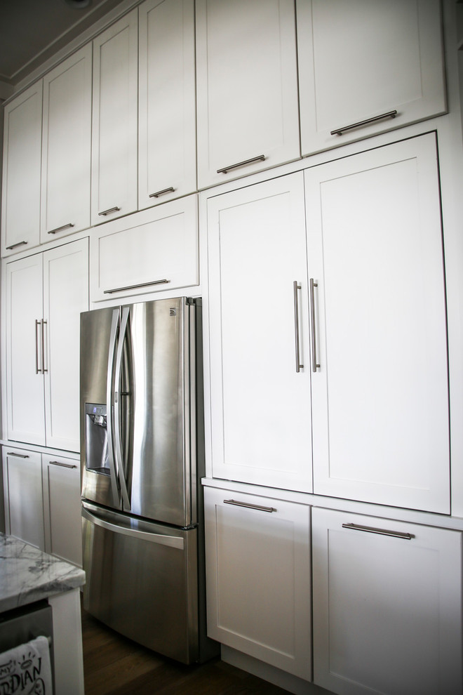 Modern inredning av ett avskilt, mellanstort flerfärgad flerfärgat u-kök, med en enkel diskho, luckor med infälld panel, vita skåp, marmorbänkskiva, grått stänkskydd, stänkskydd i metallkakel, rostfria vitvaror, plywoodgolv, en köksö och brunt golv