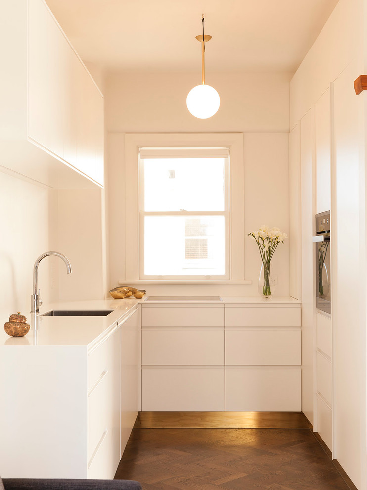 Moderne Küche in L-Form mit Unterbauwaschbecken, flächenbündigen Schrankfronten, weißen Schränken, dunklem Holzboden und Kücheninsel in Auckland