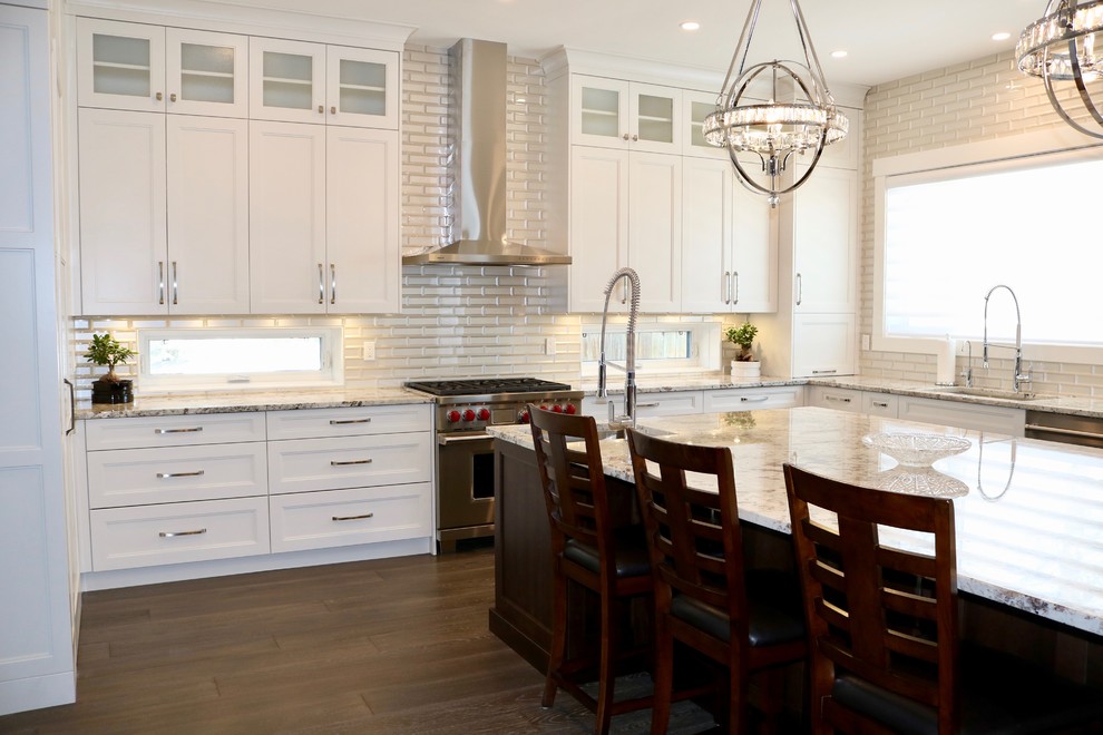 Example of a large trendy l-shaped medium tone wood floor and brown floor kitchen design in Calgary with a drop-in sink, shaker cabinets, white cabinets, granite countertops, white backsplash, glass tile backsplash, stainless steel appliances, an island and yellow countertops