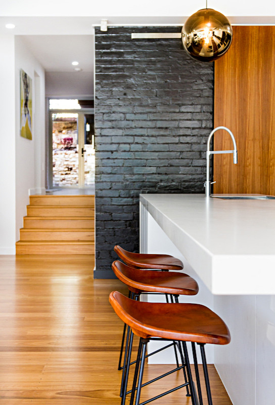 Design ideas for an expansive contemporary galley open plan kitchen in Brisbane with a built-in sink, flat-panel cabinets, white cabinets, engineered stone countertops, black splashback, marble splashback, stainless steel appliances, medium hardwood flooring, an island, brown floors and white worktops.