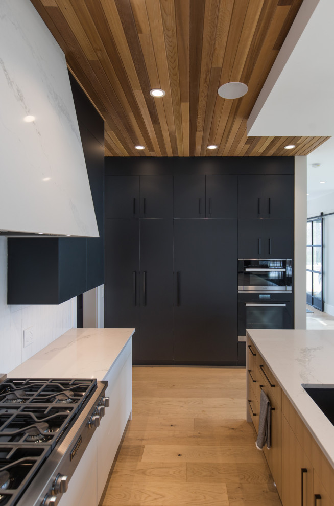 Foto på ett stort funkis flerfärgad kök, med en nedsänkt diskho, släta luckor, svarta skåp, marmorbänkskiva, vitt stänkskydd, vita vitvaror, ljust trägolv, flera köksöar och brunt golv