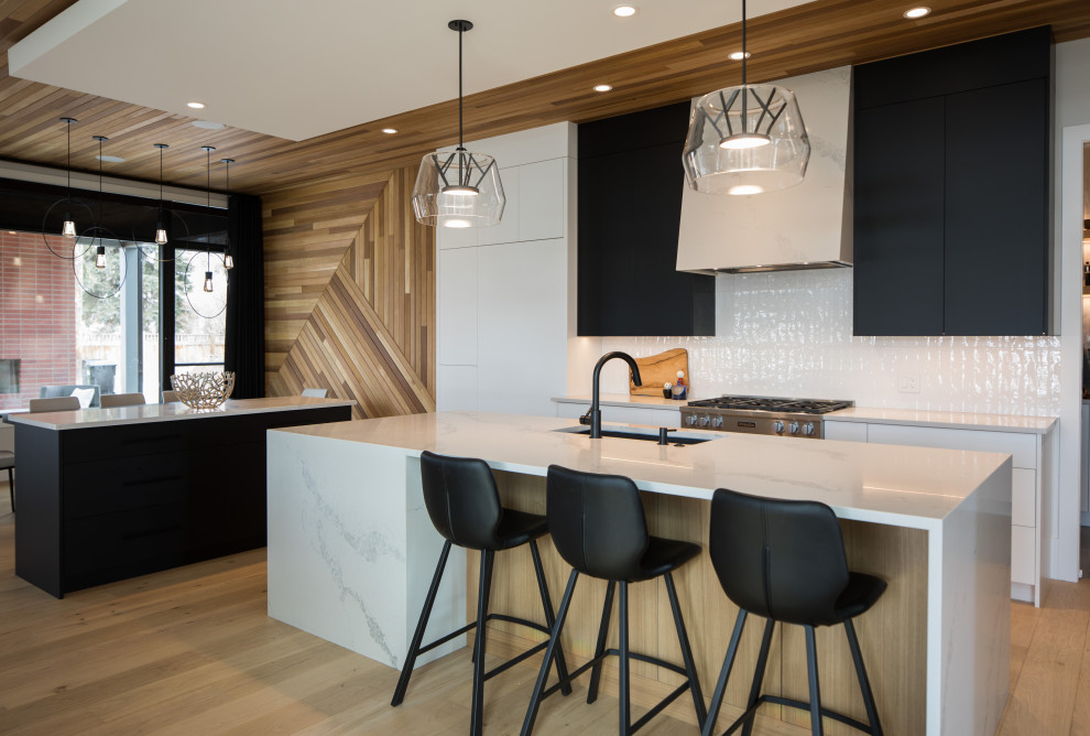 Photo of a large contemporary kitchen/diner in Calgary with flat-panel cabinets, black cabinets, white splashback, light hardwood flooring, multiple islands, a wood ceiling, a submerged sink, stainless steel appliances and white worktops.