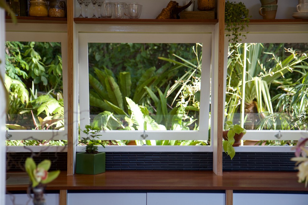 Bild på ett litet funkis linjärt kök med öppen planlösning, med en enkel diskho, vita skåp, träbänkskiva, svart stänkskydd, stänkskydd i keramik, rostfria vitvaror och mörkt trägolv