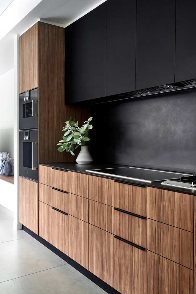 シドニーにあるコンテンポラリースタイルのおしゃれなキッチン (フラットパネル扉のキャビネット、中間色木目調キャビネット、黒いキッチンパネル、黒い調理設備、グレーの床、黒いキッチンカウンター、磁器タイルの床) の写真