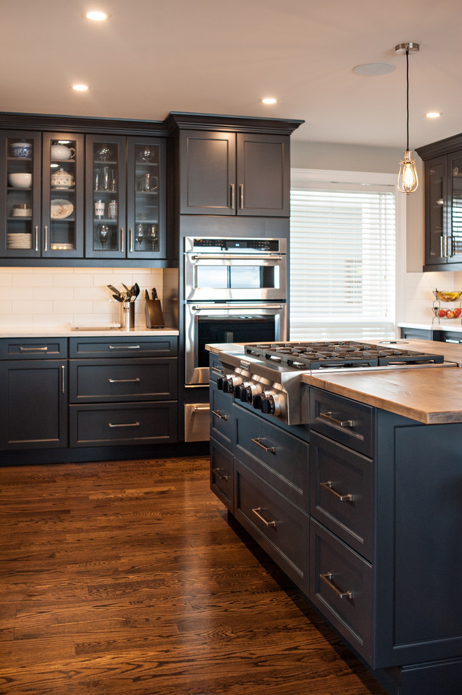 Inredning av ett modernt mellanstort kök, med en undermonterad diskho, skåp i shakerstil, blå skåp, granitbänkskiva, vitt stänkskydd, stänkskydd i tunnelbanekakel, rostfria vitvaror, mellanmörkt trägolv och en köksö
