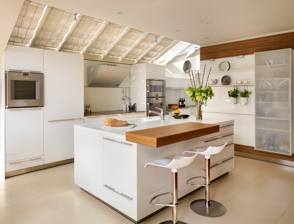 Foto på ett stort funkis kök, med rostfria vitvaror, träbänkskiva, släta luckor, vita skåp, en dubbel diskho, vitt stänkskydd, glaspanel som stänkskydd, klinkergolv i porslin och en köksö