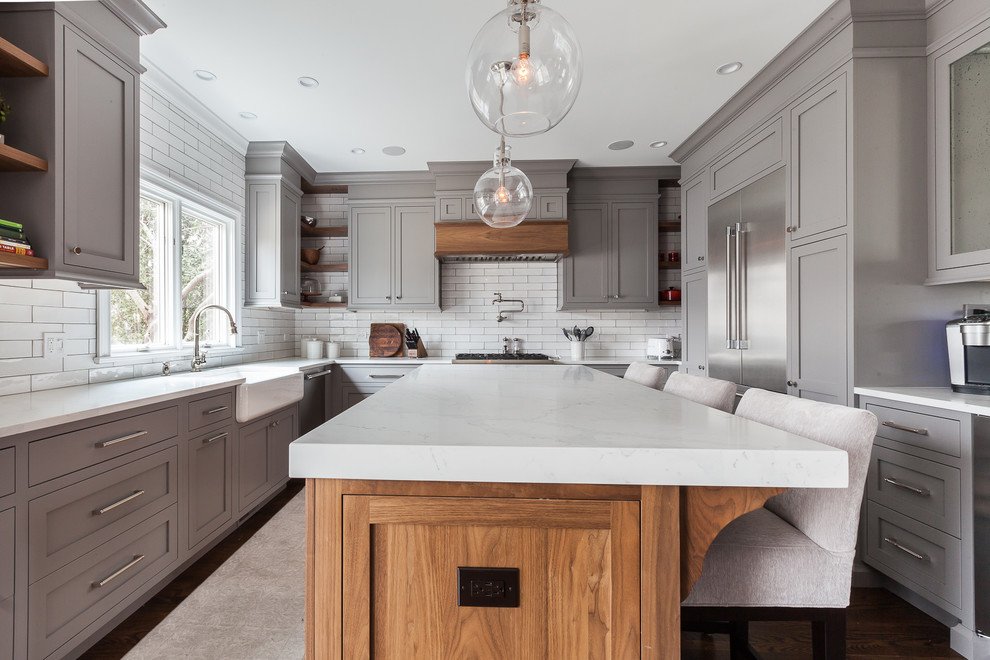 Exempel på ett stort lantligt vit vitt kök, med en rustik diskho, luckor med infälld panel, skåp i mellenmörkt trä, bänkskiva i kvarts, vitt stänkskydd, stänkskydd i porslinskakel, rostfria vitvaror, mellanmörkt trägolv, en köksö och brunt golv