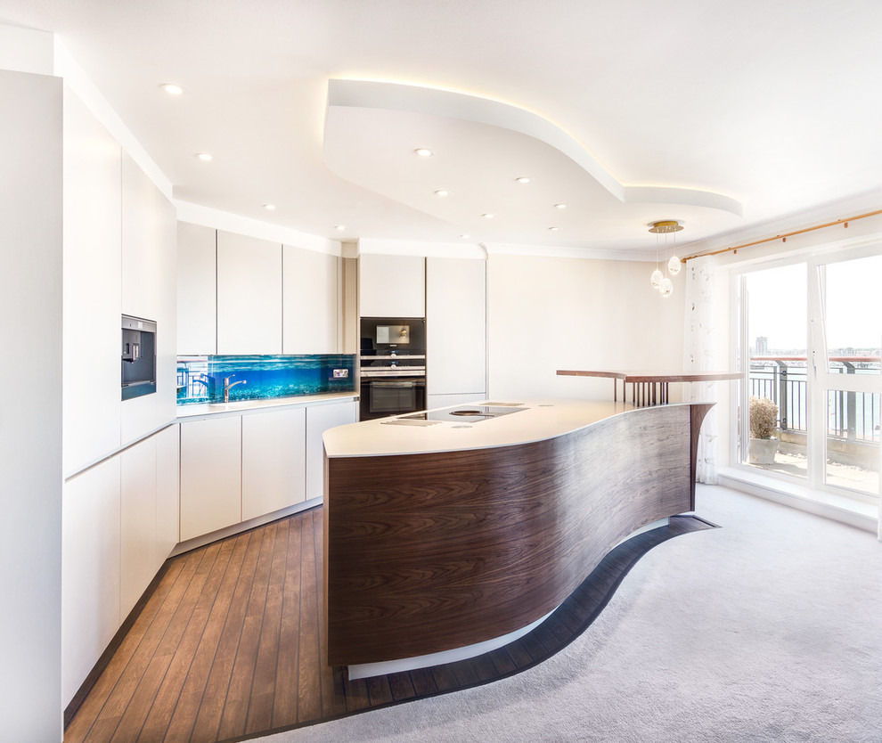 This is an example of a small beach style galley kitchen/diner in Hampshire with an integrated sink, flat-panel cabinets, grey cabinets, composite countertops, multi-coloured splashback, glass sheet splashback, stainless steel appliances, dark hardwood flooring, an island and brown floors.