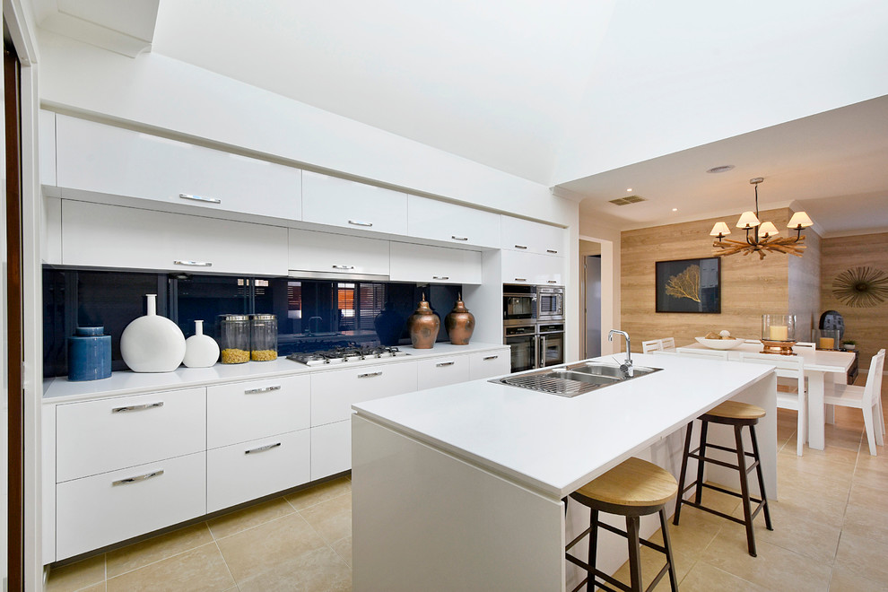 メルボルンにあるコンテンポラリースタイルのおしゃれなキッチン (ダブルシンク、フラットパネル扉のキャビネット、白いキャビネット、青いキッチンパネル、ガラス板のキッチンパネル、シルバーの調理設備) の写真