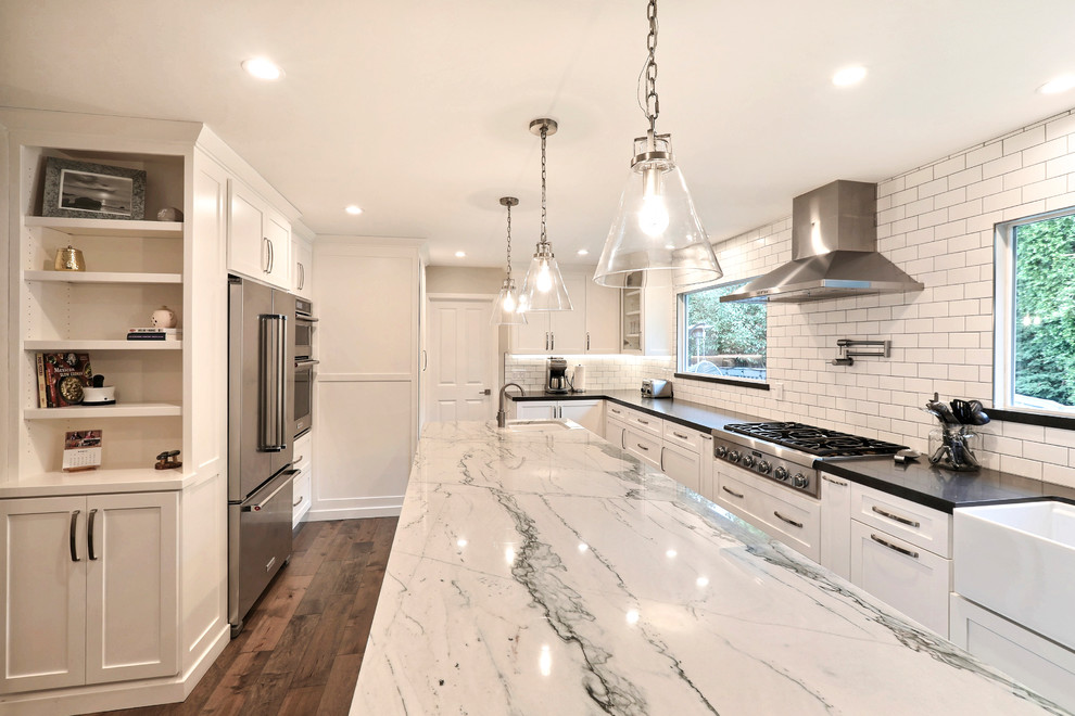Example of a large transitional l-shaped medium tone wood floor and brown floor eat-in kitchen design in San Francisco with a farmhouse sink, shaker cabinets, white cabinets, quartz countertops, white backsplash, subway tile backsplash, stainless steel appliances, an island and black countertops