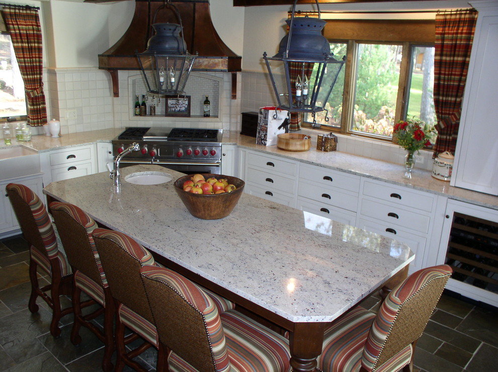 Photo of a medium sized country l-shaped enclosed kitchen in Detroit with a belfast sink, beaded cabinets, white cabinets, granite worktops, white splashback, ceramic splashback, slate flooring, an island, stainless steel appliances and grey floors.