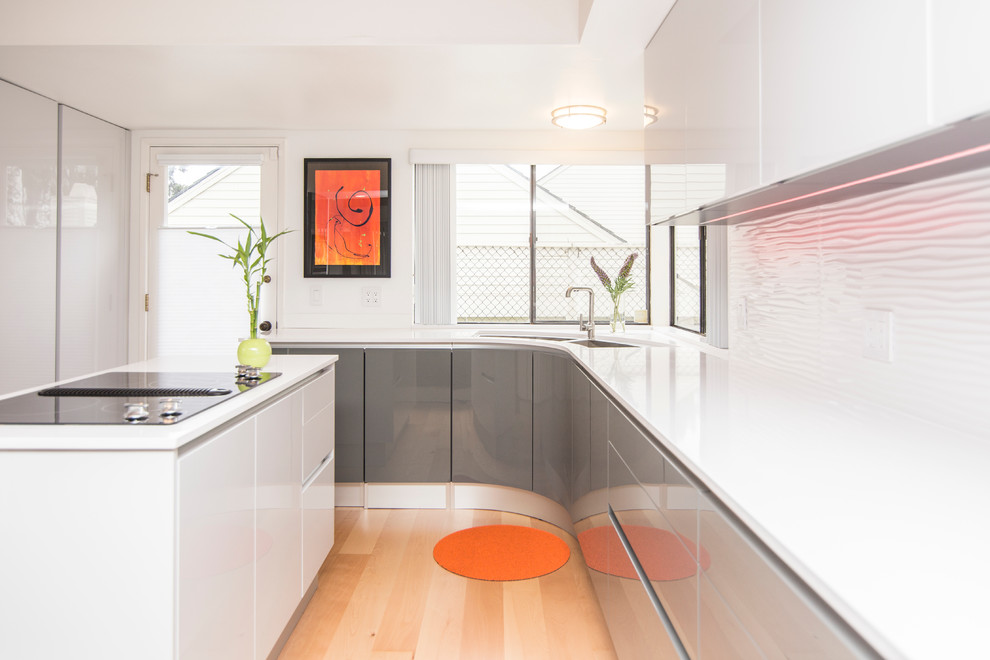 Mittelgroße Moderne Wohnküche mit Doppelwaschbecken, flächenbündigen Schrankfronten, grauen Schränken, Küchenrückwand in Weiß, hellem Holzboden und Kücheninsel in San Diego