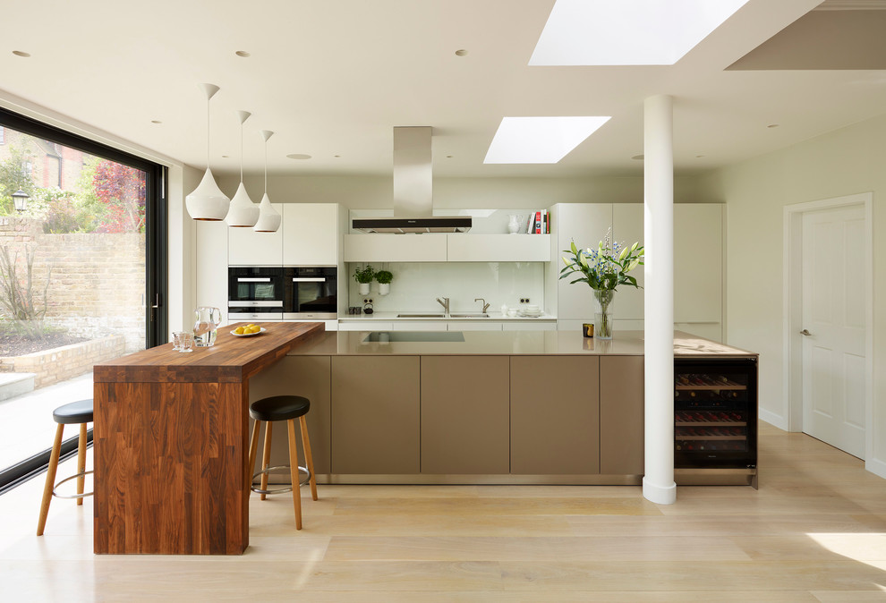 Einzeilige Moderne Küche mit flächenbündigen Schrankfronten, weißen Schränken, Küchenrückwand in Weiß, Küchengeräten aus Edelstahl, hellem Holzboden und Kücheninsel in Sonstige