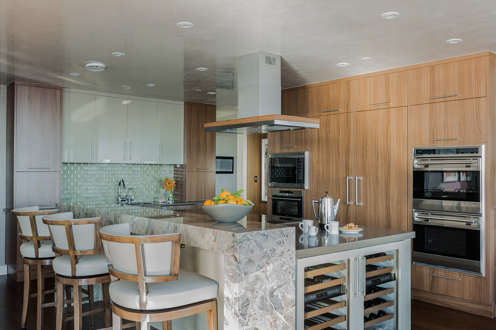 Mid-sized transitional l-shaped medium tone wood floor open concept kitchen photo in Boston with flat-panel cabinets, medium tone wood cabinets, solid surface countertops, green backsplash, glass tile backsplash, stainless steel appliances and an island