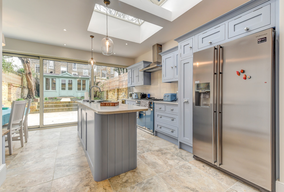 Photo of a large traditional galley kitchen/diner in London with a submerged sink, shaker cabinets, blue cabinets, grey splashback, stainless steel appliances, porcelain flooring, an island, beige floors and grey worktops.