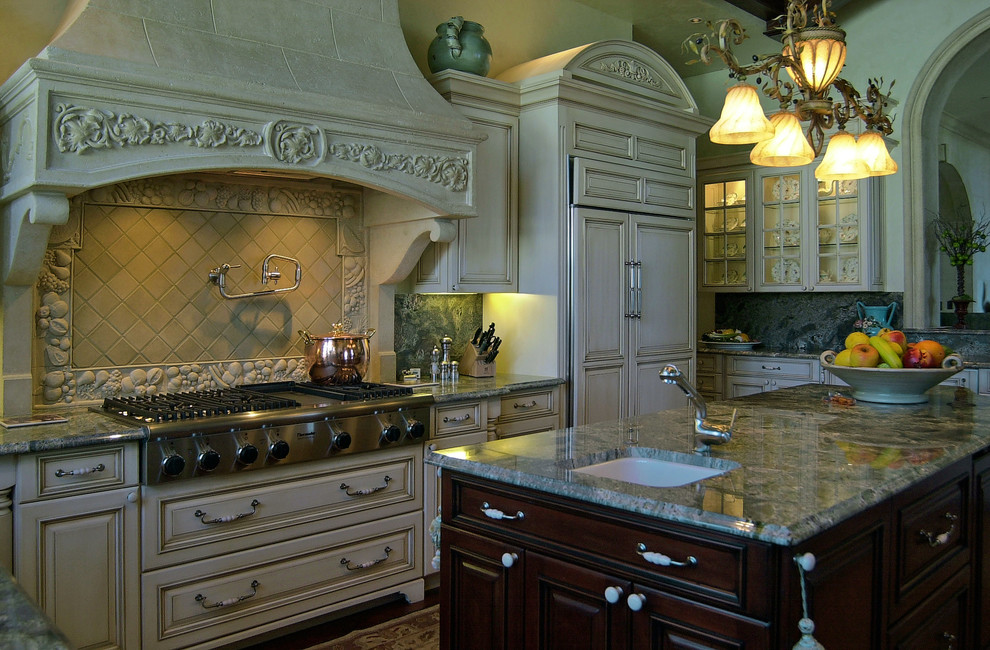 This is an example of a large mediterranean u-shaped enclosed kitchen in Tampa with a submerged sink, raised-panel cabinets, distressed cabinets, beige splashback, ceramic splashback, integrated appliances, dark hardwood flooring, an island, brown floors and grey worktops.