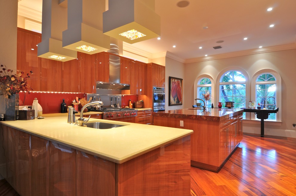 Immagine di una grande cucina contemporanea con lavello da incasso, ante lisce, ante in legno scuro, paraspruzzi rosso, elettrodomestici in acciaio inossidabile e pavimento in legno massello medio