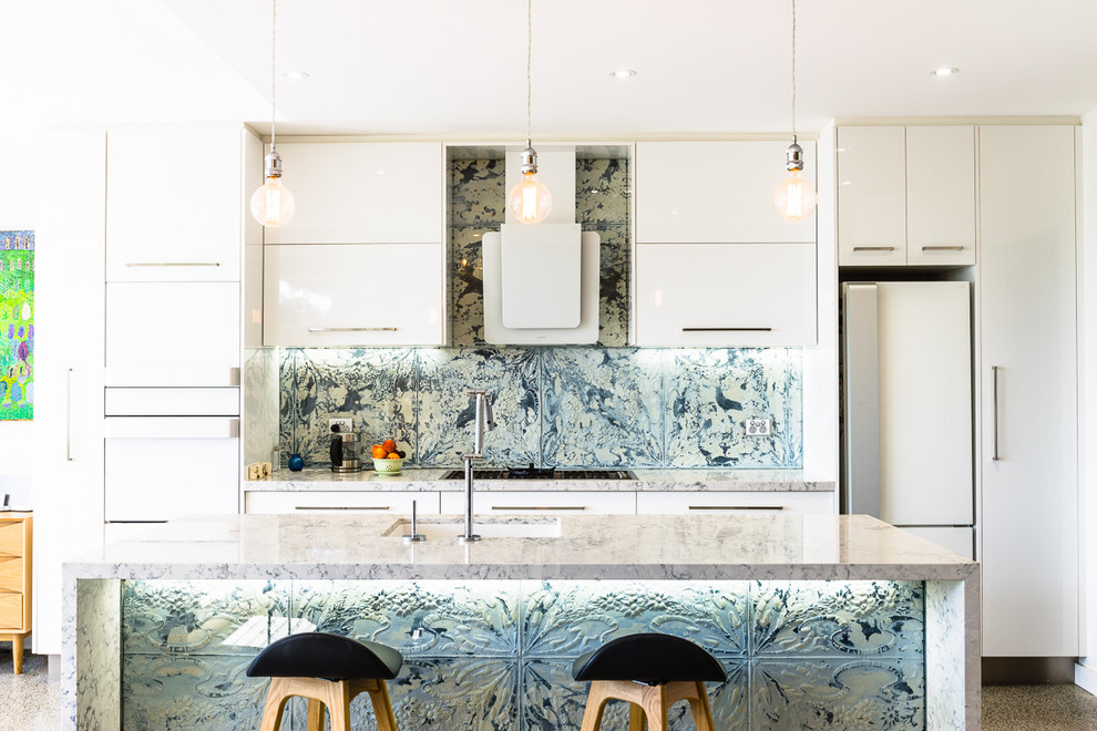 Contemporary galley kitchen in Sydney with a submerged sink, flat-panel cabinets, white cabinets, metallic splashback, white appliances, an island, brown floors and grey worktops.