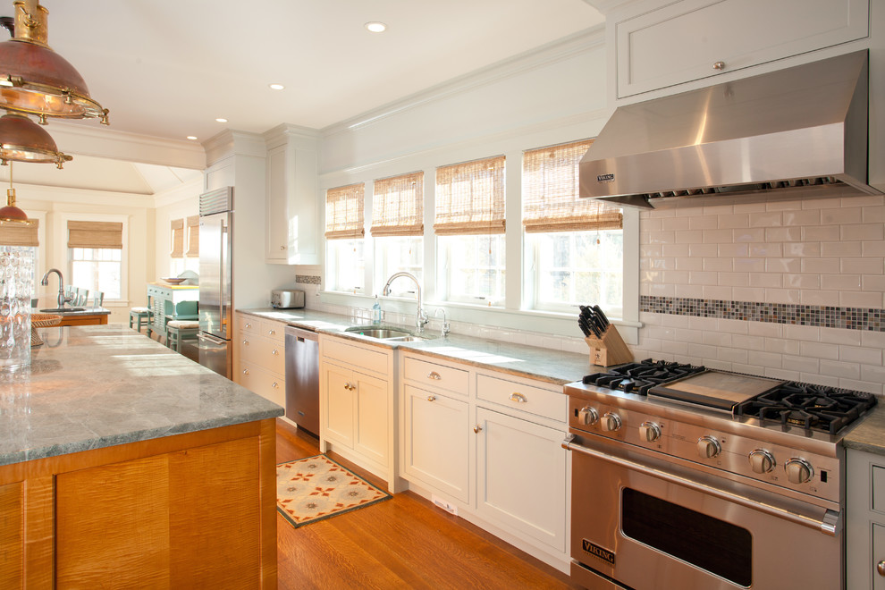 Große Maritime Wohnküche in L-Form mit Doppelwaschbecken, weißen Schränken, Glas-Arbeitsplatte, Küchenrückwand in Weiß, Rückwand aus Keramikfliesen, Küchengeräten aus Edelstahl, hellem Holzboden und zwei Kücheninseln in Boston
