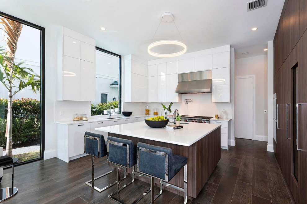 Große Moderne Küche in U-Form mit Unterbauwaschbecken, flächenbündigen Schrankfronten, weißen Schränken, Küchenrückwand in Weiß, Elektrogeräten mit Frontblende, Kücheninsel, braunem Boden und weißer Arbeitsplatte in Miami