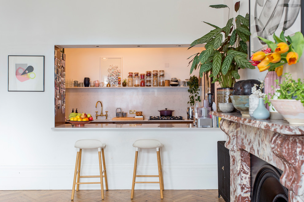 Design ideas for a bohemian galley kitchen in London with a submerged sink, quartz worktops, white splashback, light hardwood flooring, a breakfast bar, brown floors and white worktops.