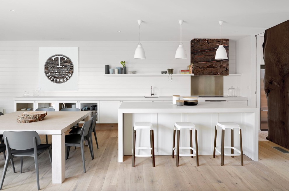 Modern inredning av ett stort kök, med en undermonterad diskho, luckor med glaspanel, vita skåp, vitt stänkskydd, stänkskydd i trä, ljust trägolv, en köksö och beiget golv