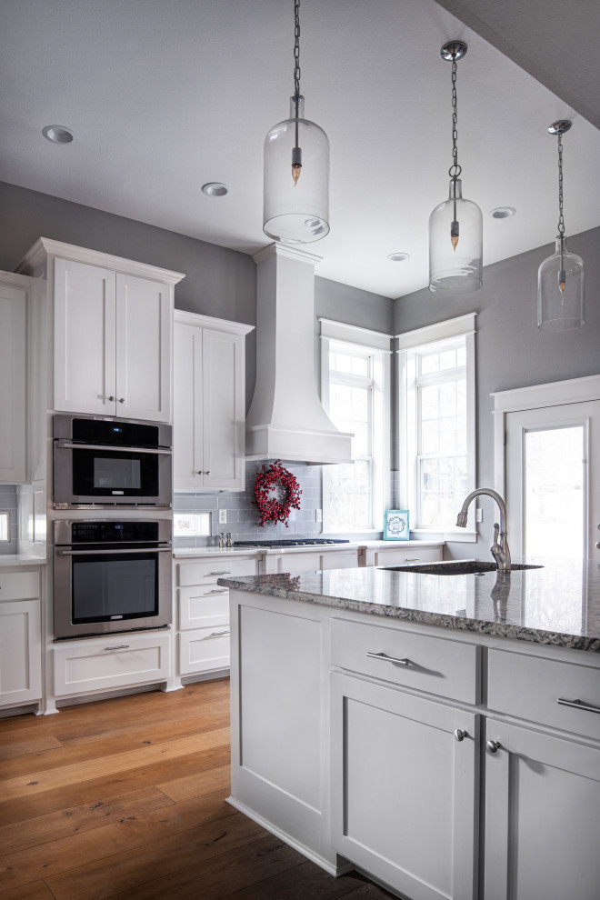 Klassisk inredning av ett mellanstort grå grått kök, med släta luckor, vita skåp, marmorbänkskiva, stänkskydd i keramik, rostfria vitvaror, mellanmörkt trägolv, en köksö, brunt golv, en enkel diskho och grått stänkskydd