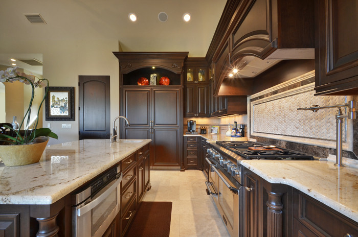 Example of a large tuscan l-shaped eat-in kitchen design in Austin with dark wood cabinets, granite countertops, multicolored backsplash, an island and raised-panel cabinets
