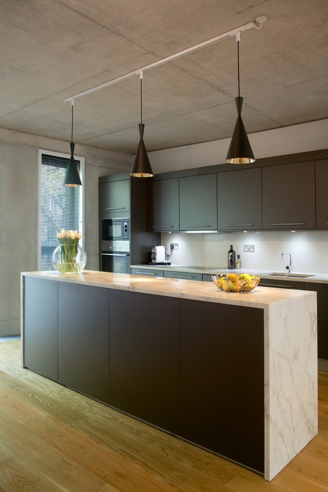 Urban galley medium tone wood floor kitchen photo in London with an undermount sink, flat-panel cabinets, brown cabinets, white backsplash, stainless steel appliances and an island