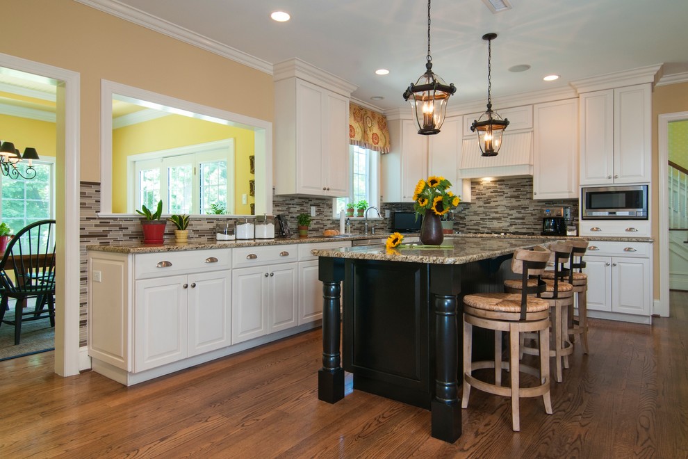 Example of a mid-sized classic l-shaped eat-in kitchen design in Philadelphia with white cabinets, granite countertops, multicolored backsplash, glass tile backsplash, stainless steel appliances, an island and raised-panel cabinets
