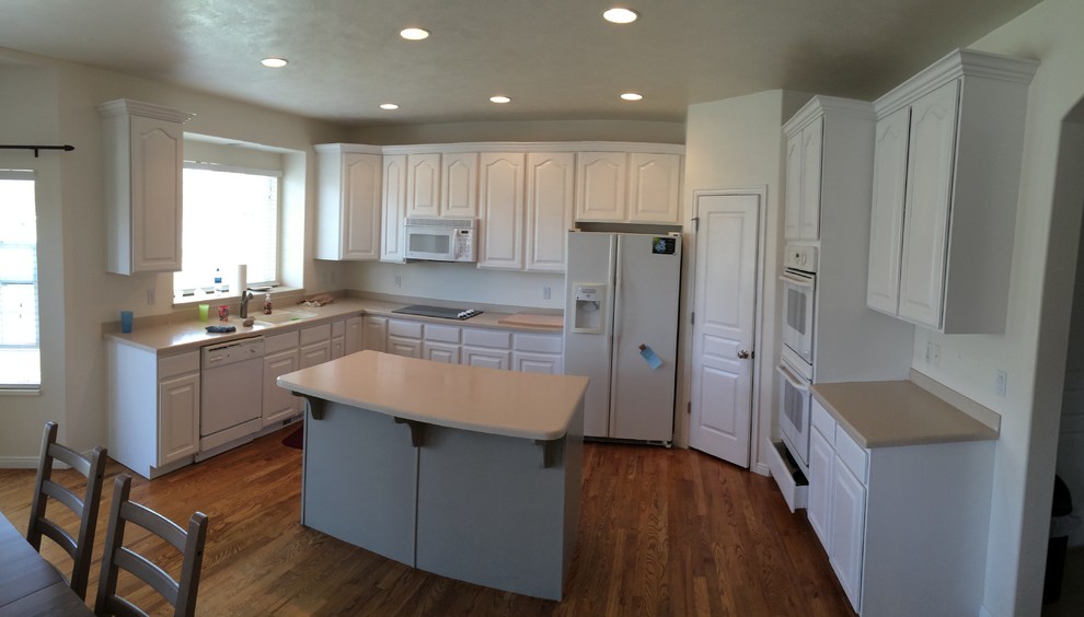 This is an example of a medium sized traditional u-shaped kitchen/diner in Austin with a double-bowl sink, raised-panel cabinets, white cabinets, composite countertops, white appliances, dark hardwood flooring, an island and brown floors.