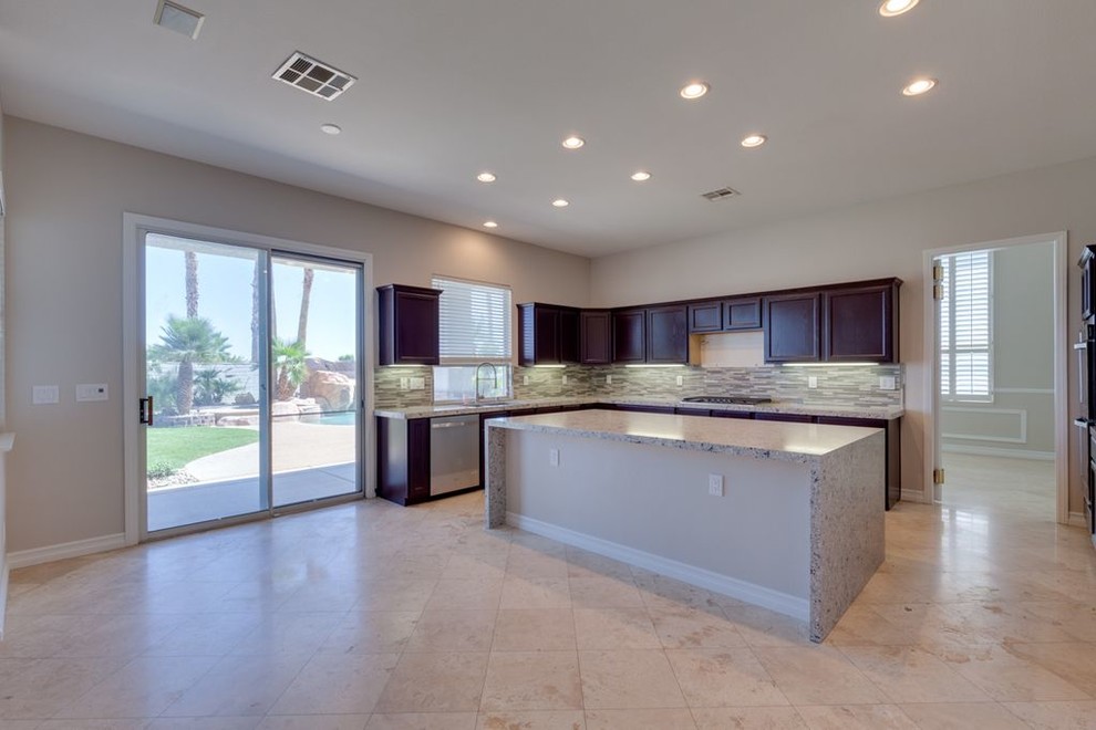 Inspiration for a large transitional l-shaped travertine floor and brown floor open concept kitchen remodel in Las Vegas with an undermount sink, recessed-panel cabinets, dark wood cabinets, granite countertops, multicolored backsplash, glass tile backsplash, an island and gray countertops