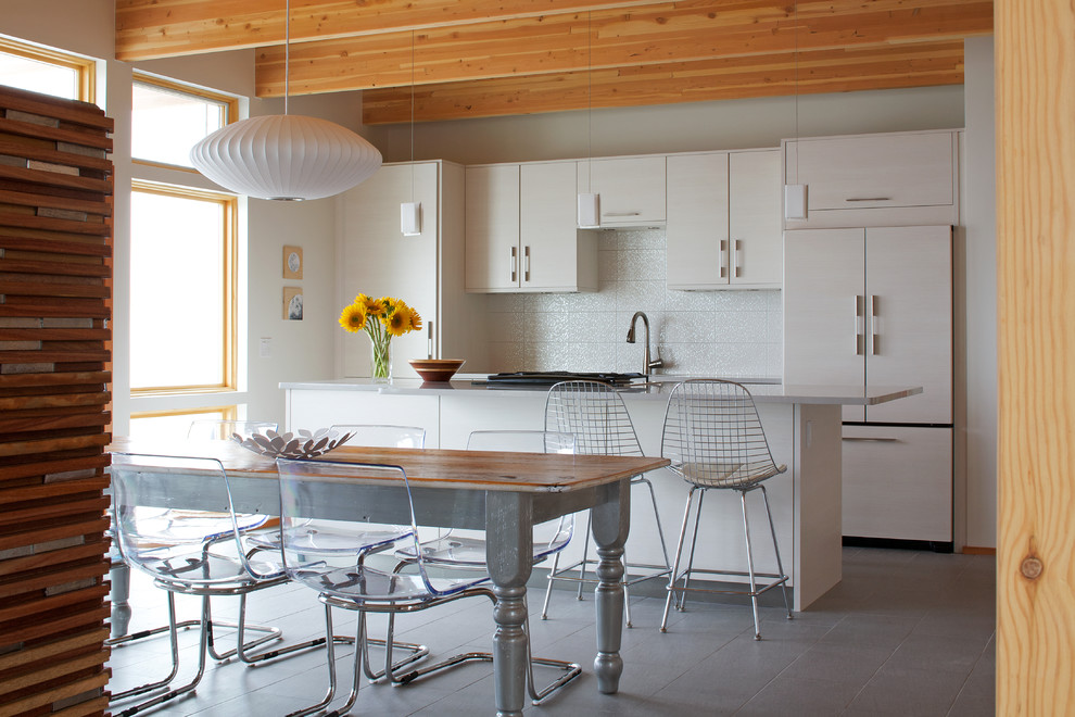 На фото: параллельная кухня среднего размера в современном стиле с обеденным столом, плоскими фасадами, белыми фасадами, белым фартуком, техникой под мебельный фасад, полом из керамической плитки и островом