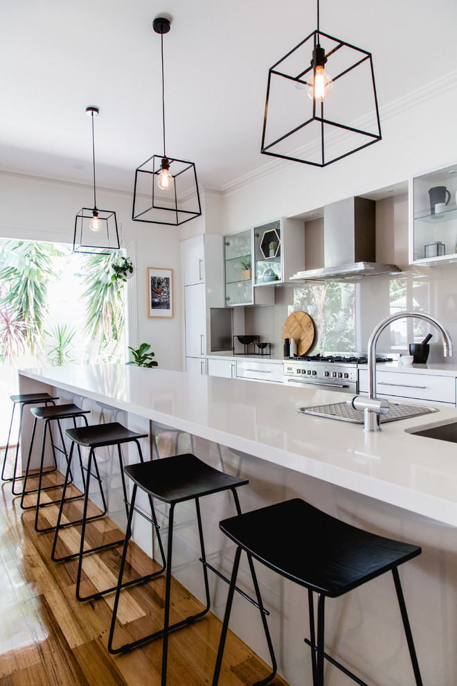 This is an example of a medium sized contemporary galley open plan kitchen in Melbourne with glass-front cabinets, grey splashback, stainless steel appliances and an island.