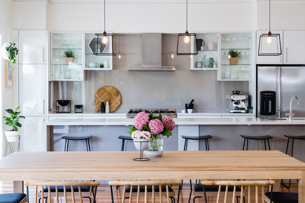 На фото: параллельная кухня-гостиная среднего размера в современном стиле с стеклянными фасадами, серым фартуком, техникой из нержавеющей стали и островом с