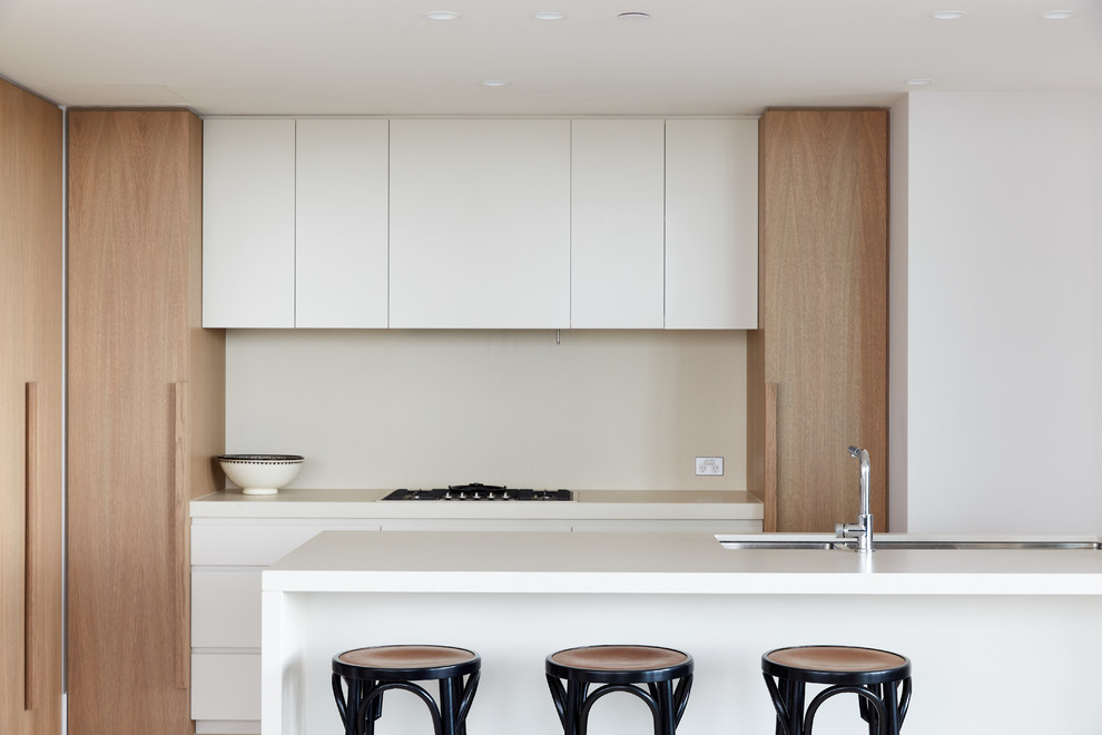 Moderne Küche mit Unterbauwaschbecken, flächenbündigen Schrankfronten, weißen Schränken, Küchenrückwand in Beige, Elektrogeräten mit Frontblende, Kücheninsel und weißer Arbeitsplatte in Melbourne