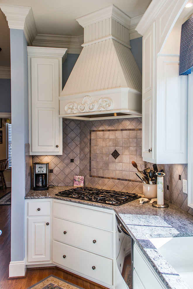 Klassisk inredning av ett mellanstort kök, med en dubbel diskho, luckor med upphöjd panel, vita skåp, granitbänkskiva, beige stänkskydd, stänkskydd i stenkakel, svarta vitvaror, mellanmörkt trägolv och en köksö