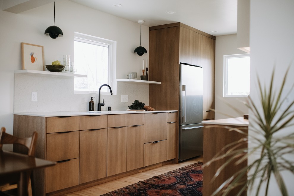 This is an example of a contemporary galley kitchen in Minneapolis with a submerged sink, flat-panel cabinets, medium wood cabinets, white splashback, stainless steel appliances, medium hardwood flooring, brown floors and white worktops.