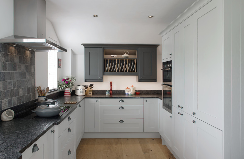 Kleine Klassische Küche ohne Insel in U-Form mit Schrankfronten im Shaker-Stil, grauen Schränken, Küchenrückwand in Grau, Küchengeräten aus Edelstahl, hellem Holzboden, beigem Boden, schwarzer Arbeitsplatte und Rückwand aus Mosaikfliesen in Cornwall