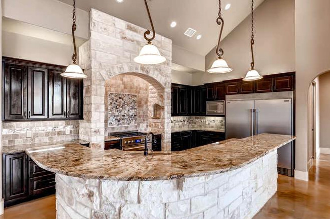 Inspiration for a large mediterranean l-shaped kitchen/diner in Austin with a single-bowl sink, raised-panel cabinets, dark wood cabinets, granite worktops, beige splashback, stone tiled splashback, stainless steel appliances, concrete flooring and an island.