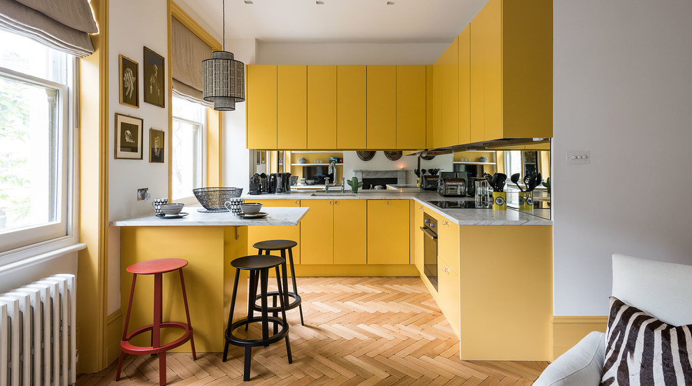 Example of a small danish l-shaped medium tone wood floor kitchen design in London with an undermount sink, flat-panel cabinets, yellow cabinets, mirror backsplash and a peninsula