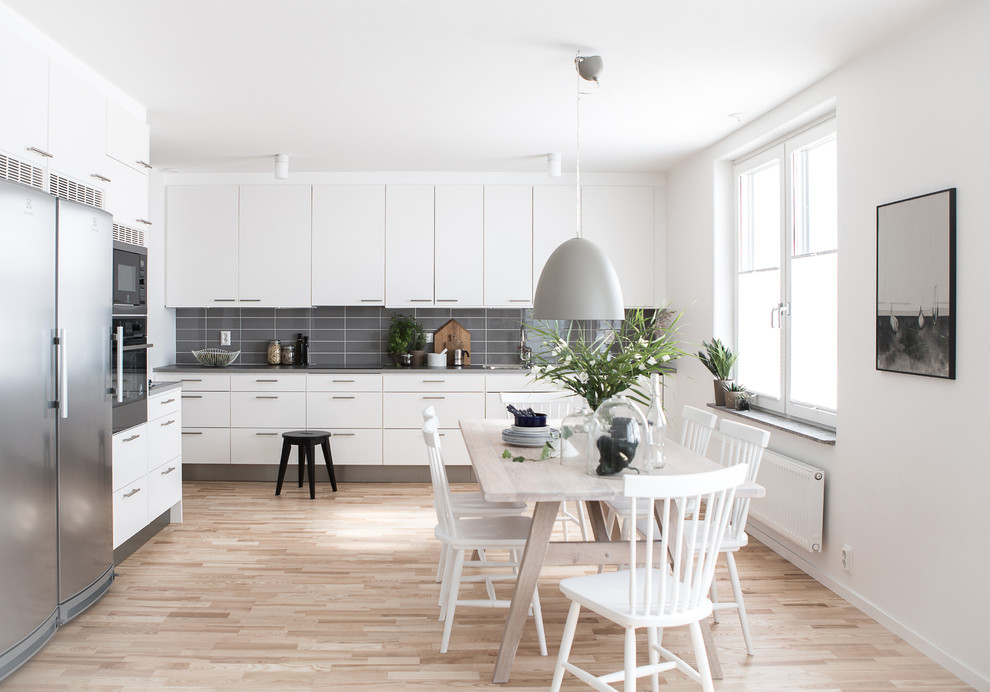 Exempel på ett mellanstort nordiskt linjärt kök och matrum, med släta luckor, vita skåp, grått stänkskydd, rostfria vitvaror och ljust trägolv